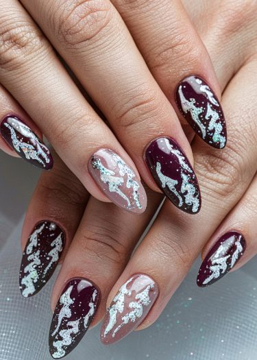 Elegant burgundy nail art with shimmering silver glitter designs and negative space details.