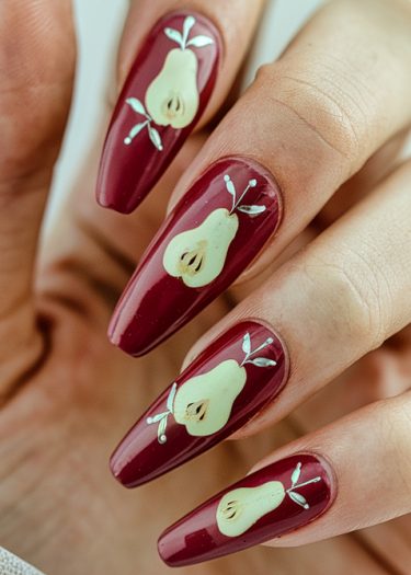 Elegant burgundy nail art featuring pear designs and metallic accents for a stylish look.