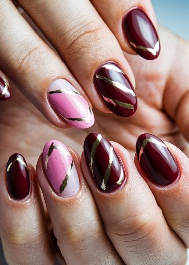 Elegant burgundy and pink nail art with gold stripes for a glamorous manicure.