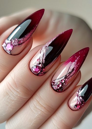 Elegant burgundy-pink ombre stiletto nails adorned with sparkling gemstones and glitter patterns.