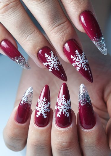 Elegant burgundy nail art with white snowflakes and silver glitter for festive holiday cheer.