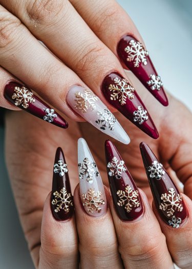 Elegant burgundy stiletto nails with metallic snowflake designs for a festive winter manicure.