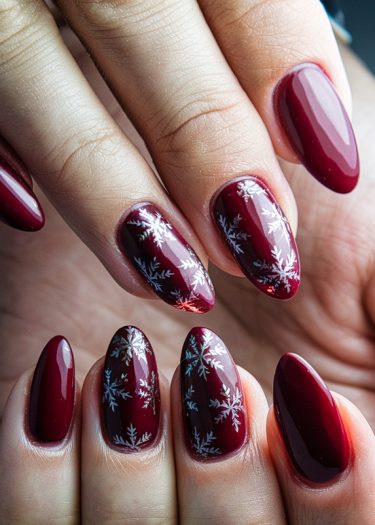 Elegant burgundy nail art with snowflakes, showcasing sophisticated almond-shaped design and glossy finish.