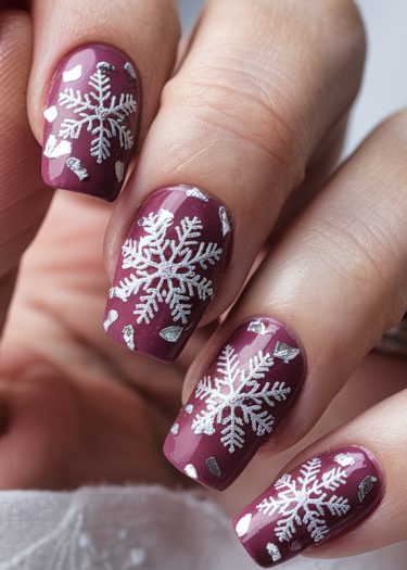 Elegant burgundy snowflake nail art with silver accents for a stylish winter look.