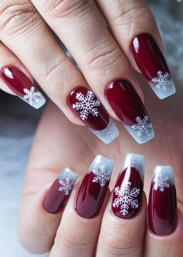 Elegant burgundy nails with detailed white snowflakes and frosted tips for winter charm.