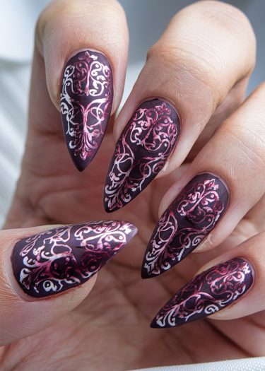 Elegant burgundy stiletto nail art with metallic rose gold filigree designs for a dramatic look.