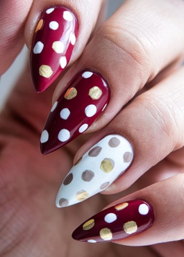 Elegant burgundy stiletto nails with gold and white polka dot designs for a modern look.