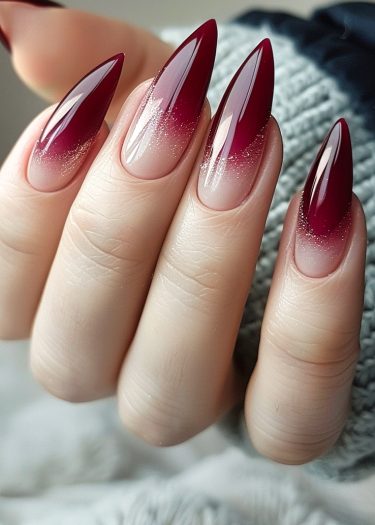 Elegant burgundy stiletto nails with ombré effect and sparkling glitter details.