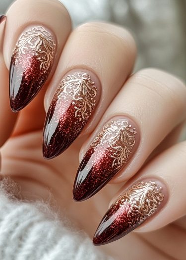 Elegant burgundy stiletto nails with gold gradient and intricate designs on a manicured hand.