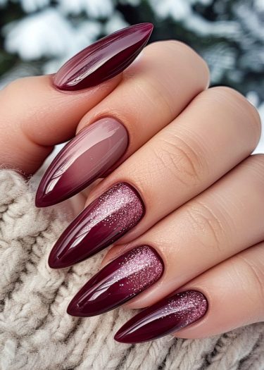 Elegant burgundy stiletto nails with glitter, cozy sweater, and wintery background.