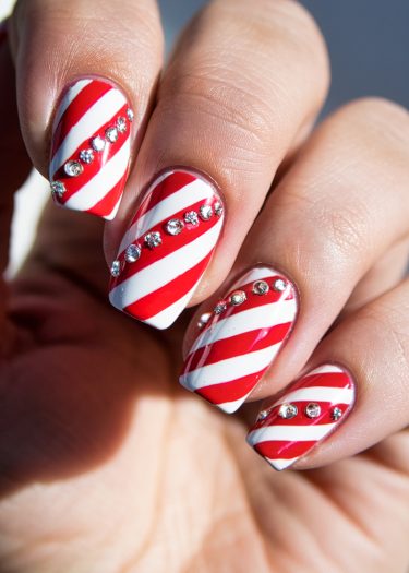 Festive candy cane nail art featuring red and white stripes with sparkling rhinestones.