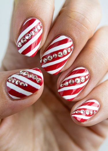 Festive candy cane nail art with red and white stripes and sparkling rhinestones.