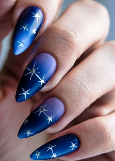 Elegant cosmic-themed nail art featuring a blue gradient and white star designs.