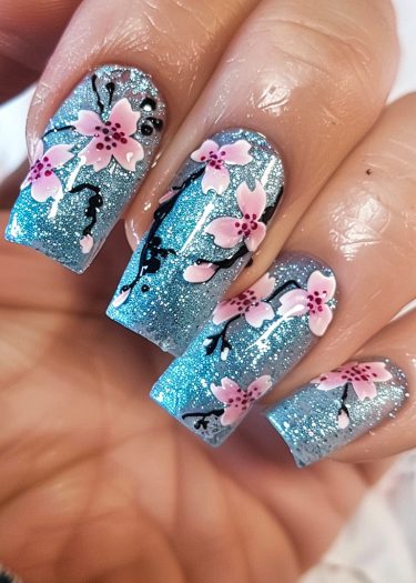 Stunning blue glitter nail art with pink cherry blossoms and black branches for a chic look.