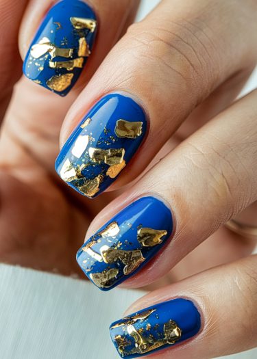 Vibrant cobalt blue squoval nails with metallic gold foil accents for elegant nail art.