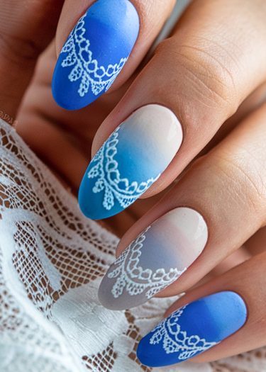 Elegant cobalt blue gradient nail art with intricate lace designs on oval-shaped nails.