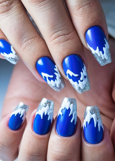 Cobalt blue wave nails with white patterns and silver glitter for stunning ocean-inspired nail art.