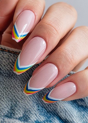 Colorful chevron nail art on long almond-shaped nails against textured denim background.