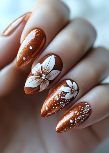 Elegant metallic copper stiletto nails featuring intricate white floral designs and decorative embellishments.