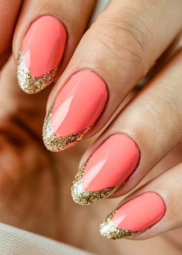 Elegant coral pink nails with gold glitter tips for a glamorous manicure.