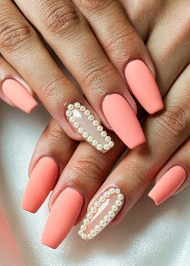 Elegant coral matte nails with pearl detailing for a sophisticated manicure look.