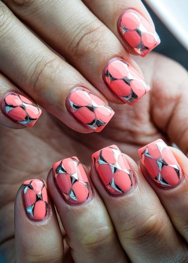 Vibrant coral nails with elegant geometric silver design and glossy finish for stylish nail art.