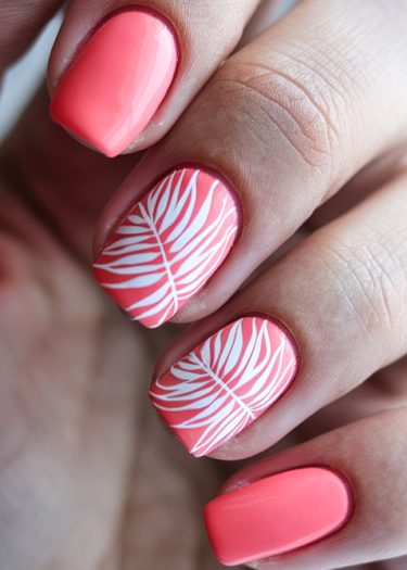 Vibrant coral-pink manicure with stylish white leaf design on polished nails.