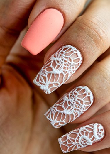 Elegant coral pink matte nails with intricate white lace designs for a sophisticated look.