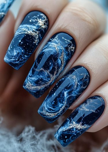 Stunning midnight blue galaxy nail art with swirling white and silver designs and glitter.