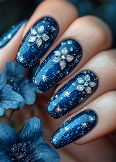 Elegant midnight blue cosmic nail design with glitter and floral accents against a soft background.