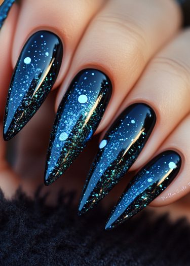 Stunning cosmic stiletto nails feature a starry night design with glittering blue accents.