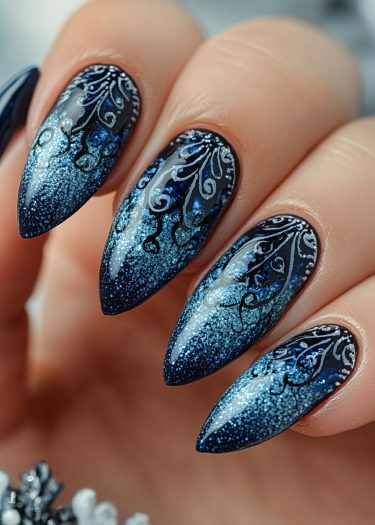 Stunning stiletto dark blue gradient nails with silver patterns and blue gems.