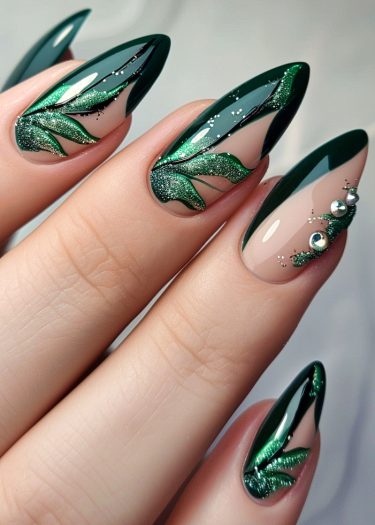 Elegant stiletto nails featuring emerald green leaf designs and sparkling embellishments for glamorous nail art.