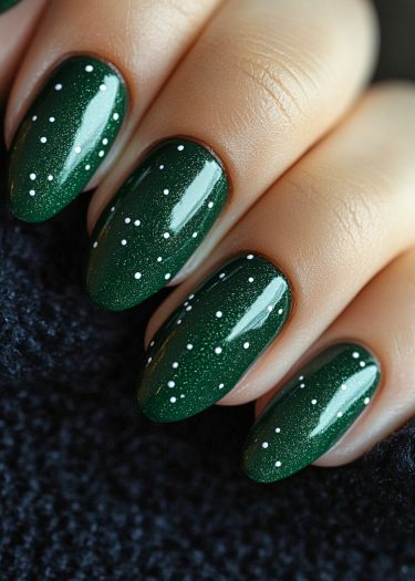 Elegant dark green nail art with white dots on almond-shaped nails against a soft background.