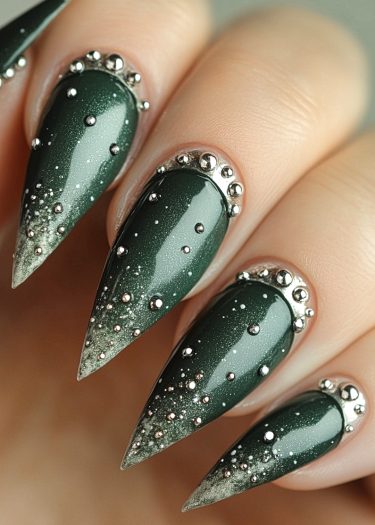 Elegant dark green stiletto nails with gradient and metallic beads for a luxurious winter look.