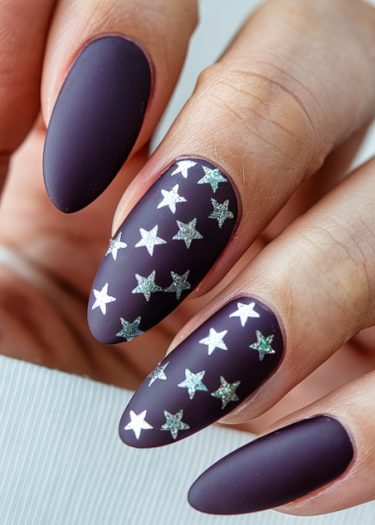 Almond-shaped matte dark purple nails with silver star designs for a chic, elegant look.