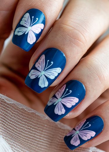 Elegant deep blue butterfly nail art design with intricate pastel details on manicured nails.