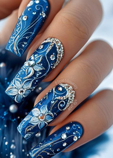 Elegant deep blue nail art with intricate floral designs and sparkling rhinestones.