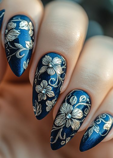 Stunning deep-blue floral nail art with metallic gold design and sparkling rhinestones.