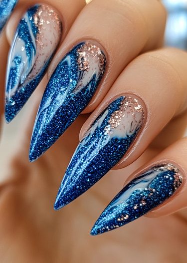 Stunning deep blue glitter stiletto nails with white marble swirls and rose gold accents.