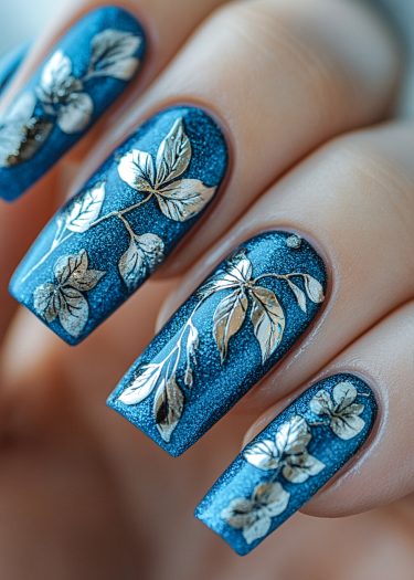 Elegant deep blue nail art with shimmering gold leaf designs for a sophisticated look.