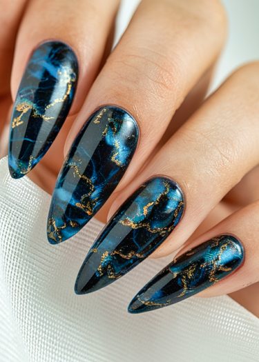 Elegant stiletto nails featuring deep blue marble patterns and luxurious gold accents.