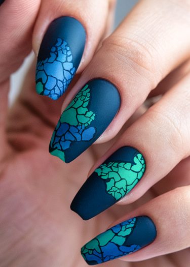 Elegant deep blue matte nail art featuring intricate abstract patterns in shades of blue and green.