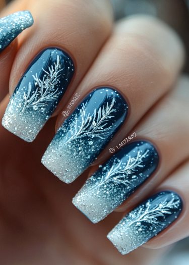 Elegant deep blue ombre nail art with silver glitter and winter branch patterns.