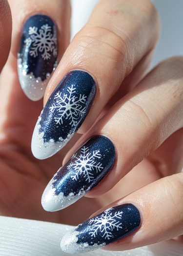 Elegant deep blue snowflake nail art with ombre tips and glitter for a winter theme.