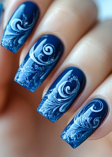 Elegant deep blue swirl nail art with intricate white designs and subtle glitter.