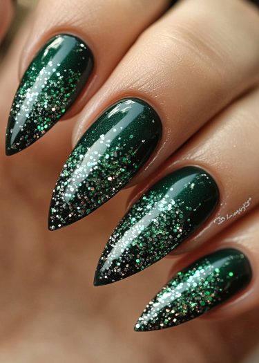 Elegant emerald green stiletto nails with sparkling gradient glitter for a glamorous manicure.