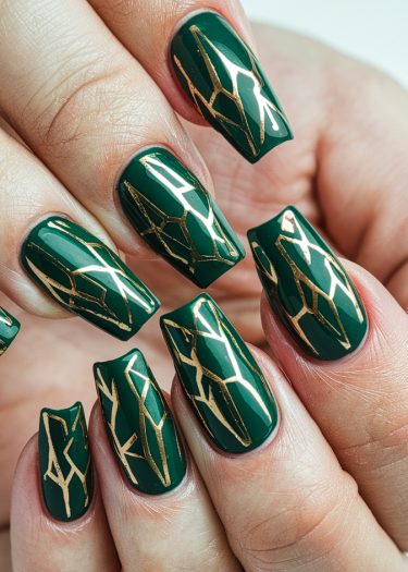 Elegant deep green nails with gold geometric designs, showcasing sophisticated nail art and grooming.