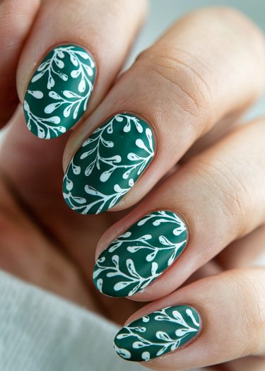 Elegant almond-shaped nails with a deep green base and intricate white leaf design.