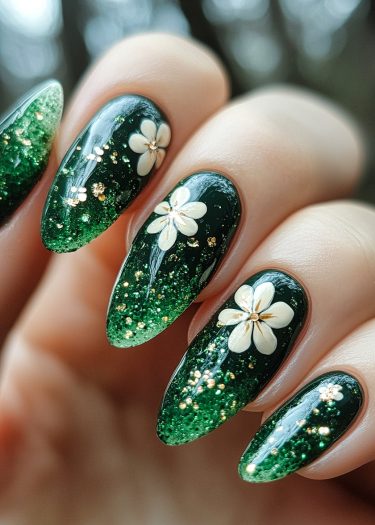 Elegant almond-shaped nails featuring deep green ombre, delicate white flowers, and golden accents.